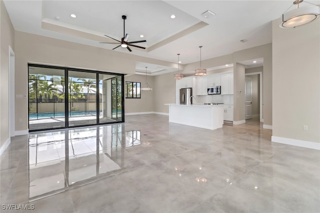 unfurnished living room with ceiling fan and a raised ceiling