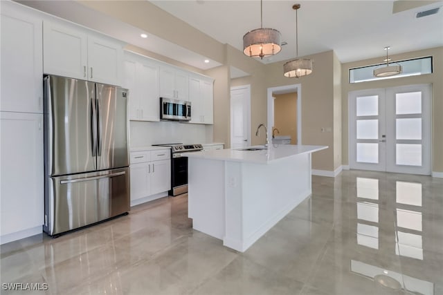 kitchen with appliances with stainless steel finishes, decorative light fixtures, white cabinets, and an island with sink