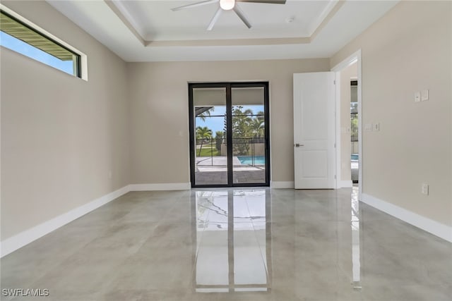 empty room with ceiling fan, a healthy amount of sunlight, and a raised ceiling