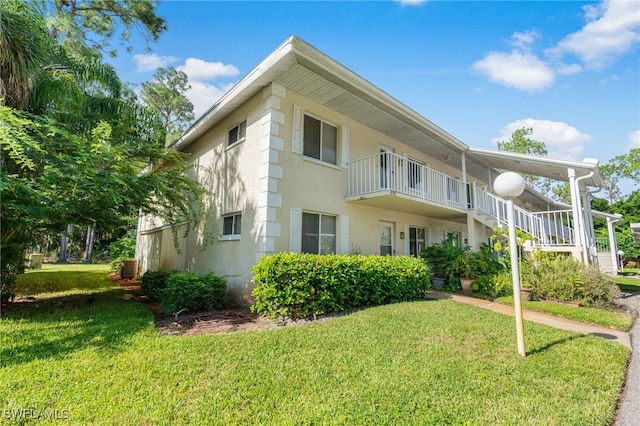 rear view of house featuring cooling unit, a lawn, and a balcony