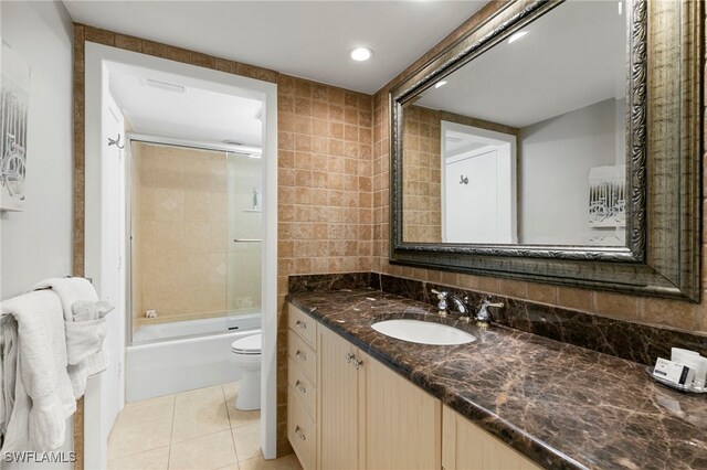 full bathroom with tile patterned floors, toilet, shower / bath combination with glass door, vanity, and tile walls