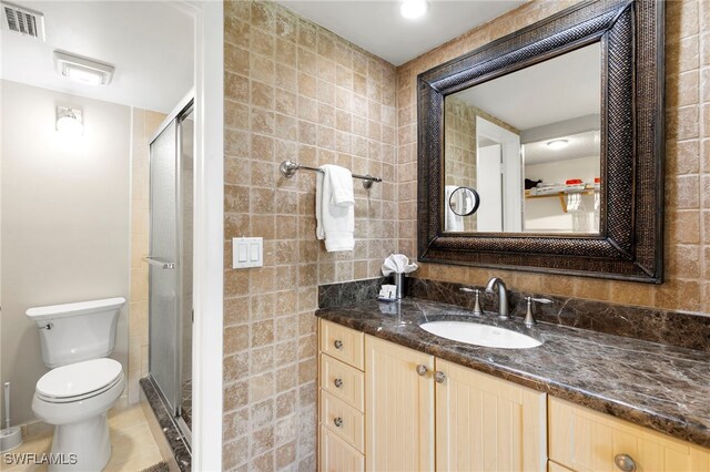 bathroom with tile patterned flooring, toilet, vanity, a shower with shower door, and tile walls