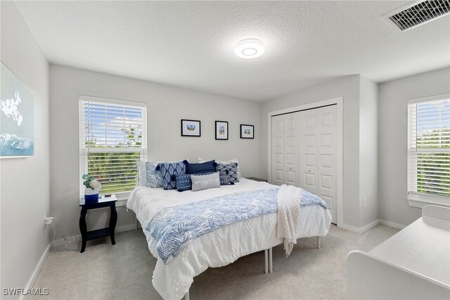 bedroom featuring a closet, light carpet, a textured ceiling, baseboards, and visible vents