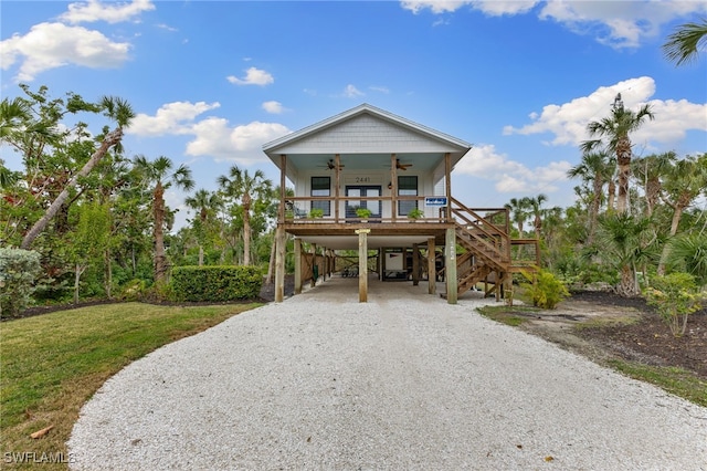 coastal home featuring gravel driveway, ceiling fan, stairway, covered porch, and a carport