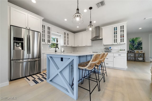kitchen with white cabinetry, light countertops, stainless steel fridge with ice dispenser, visible vents, and wall chimney range hood