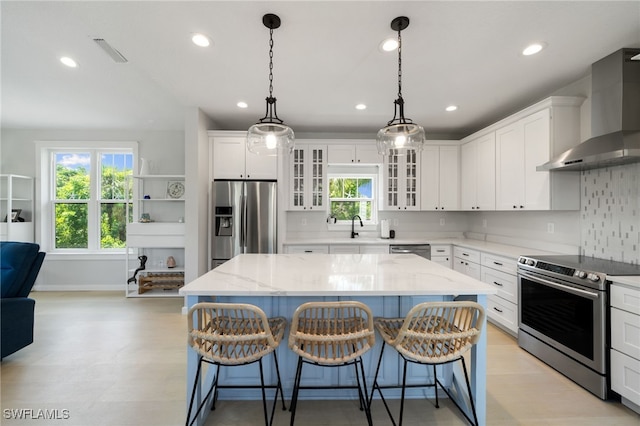 kitchen with visible vents, plenty of natural light, wall chimney exhaust hood, appliances with stainless steel finishes, and a center island