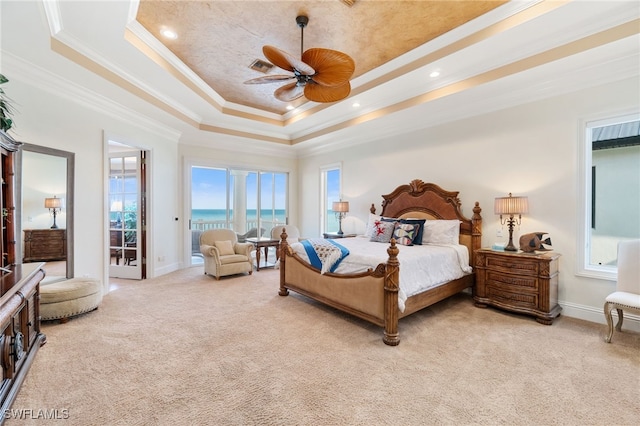 carpeted bedroom with a water view, a tray ceiling, access to exterior, ceiling fan, and ornamental molding