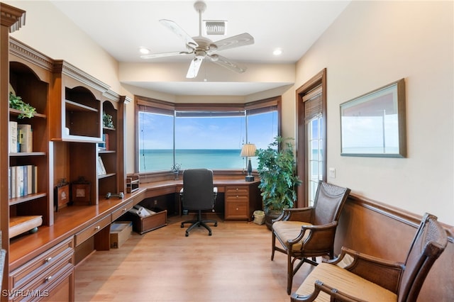 office space featuring a water view, built in desk, ceiling fan, and light hardwood / wood-style floors