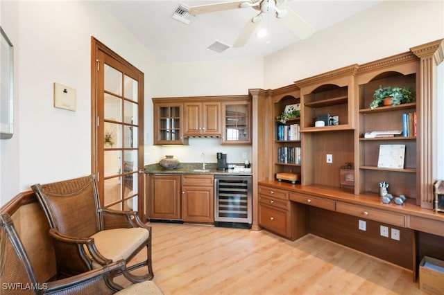 home office with indoor wet bar, light wood finished floors, built in study area, a sink, and beverage cooler