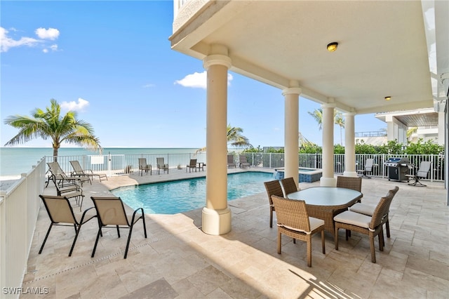 view of pool featuring a water view, a patio area, a pool with connected hot tub, and fence