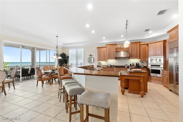 kitchen featuring a center island with sink, built in appliances, decorative light fixtures, and a water view