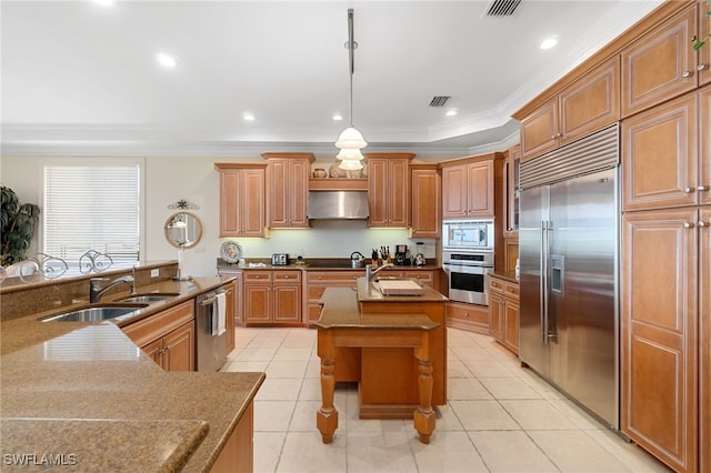 kitchen featuring hanging light fixtures, a kitchen island with sink, a sink, built in appliances, and under cabinet range hood