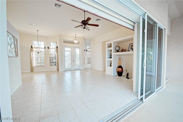 unfurnished living room with light tile patterned floors, ceiling fan with notable chandelier, and french doors