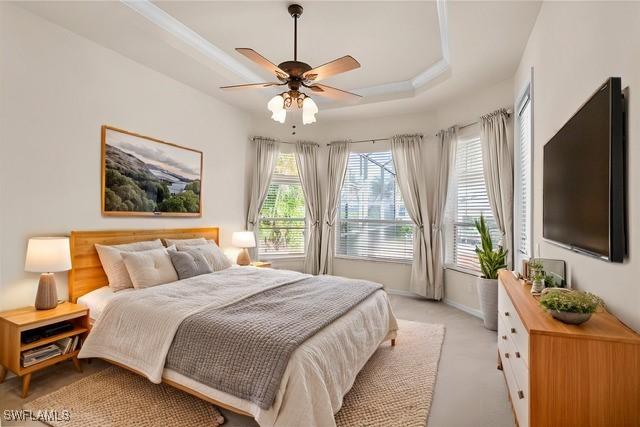 bedroom featuring ceiling fan, light colored carpet, and a raised ceiling