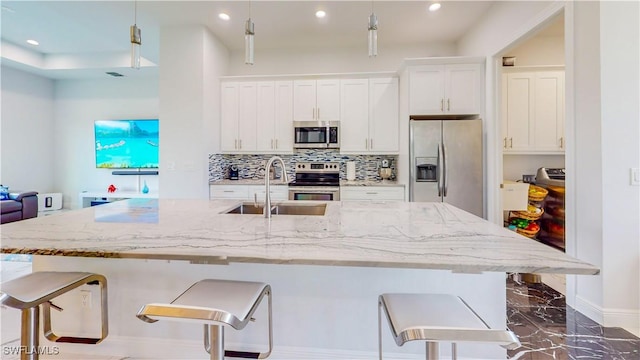 kitchen featuring backsplash, appliances with stainless steel finishes, white cabinets, a sink, and a kitchen bar