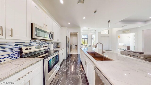 kitchen with white cabinetry, backsplash, decorative light fixtures, sink, and appliances with stainless steel finishes