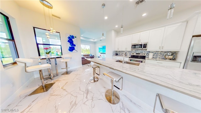 kitchen with decorative light fixtures, appliances with stainless steel finishes, white cabinetry, a breakfast bar area, and tasteful backsplash