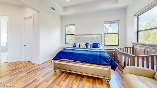 bedroom with a raised ceiling, wood finished floors, visible vents, and baseboards