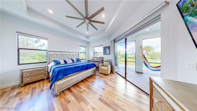 bedroom featuring light wood-type flooring, access to outside, a tray ceiling, and ceiling fan