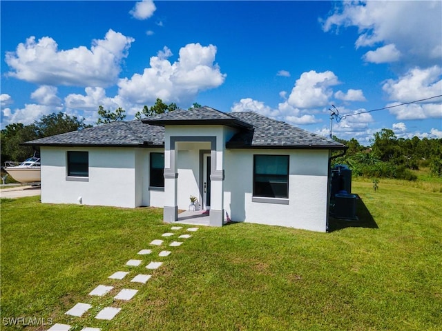 rear view of property featuring roof with shingles, a yard, and stucco siding