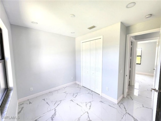 unfurnished bedroom featuring marble finish floor, baseboards, visible vents, and a closet