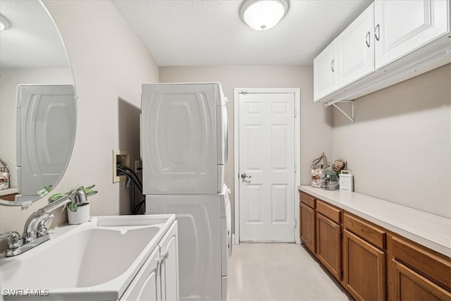 clothes washing area featuring cabinets, stacked washer and clothes dryer, and sink