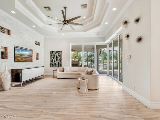 living room featuring ceiling fan, a raised ceiling, light wood-type flooring, and crown molding