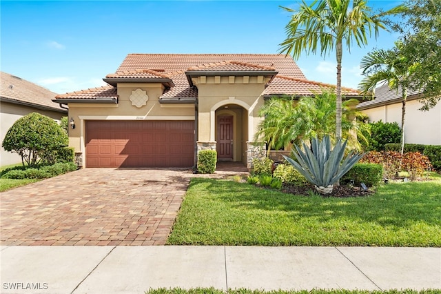 mediterranean / spanish house featuring an attached garage, a tiled roof, decorative driveway, stucco siding, and a front lawn