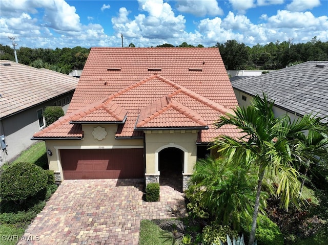 mediterranean / spanish home with a garage, stone siding, a tile roof, decorative driveway, and stucco siding