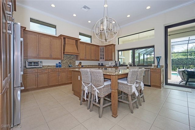 kitchen with light stone counters, premium range hood, stainless steel appliances, a notable chandelier, and crown molding