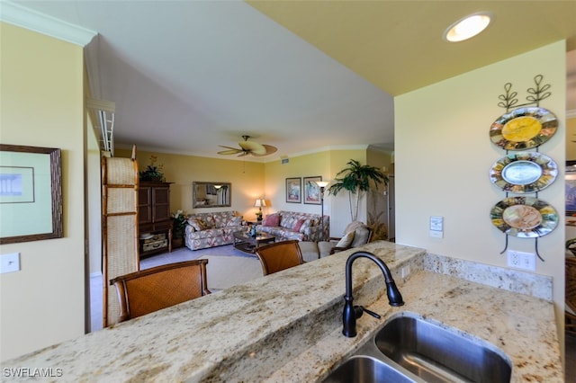 kitchen with sink, ceiling fan, light stone counters, and crown molding