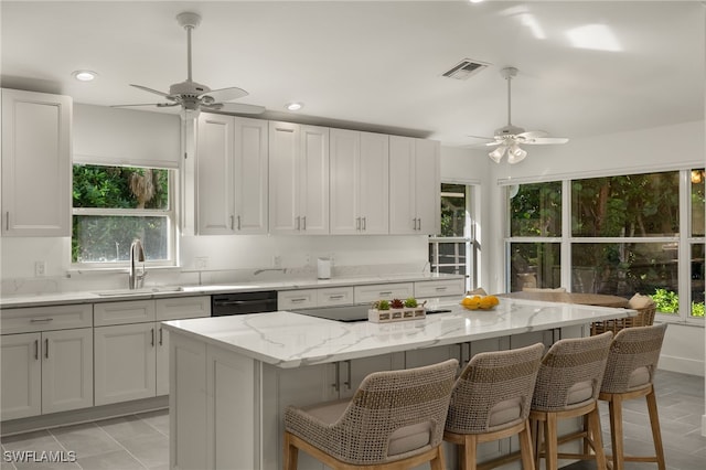 kitchen featuring visible vents, black appliances, a sink, a breakfast bar area, and light stone countertops