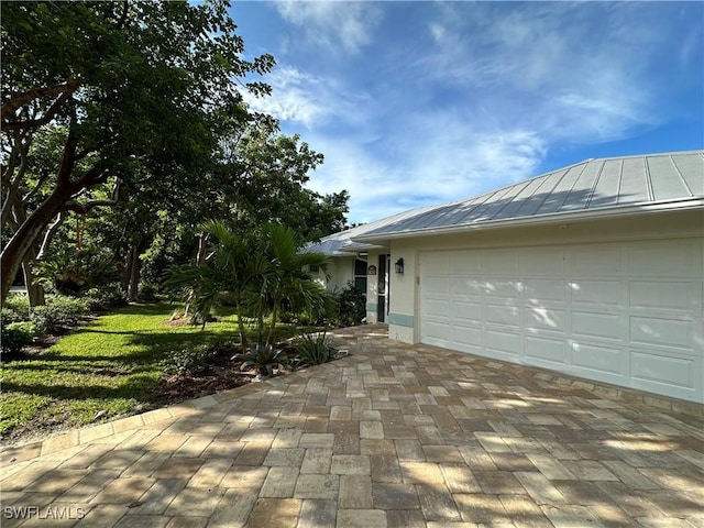 view of front of property featuring stucco siding, metal roof, decorative driveway, an attached garage, and a standing seam roof