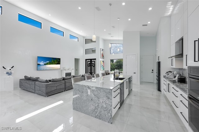 kitchen with white cabinetry, a towering ceiling, a spacious island, and decorative light fixtures