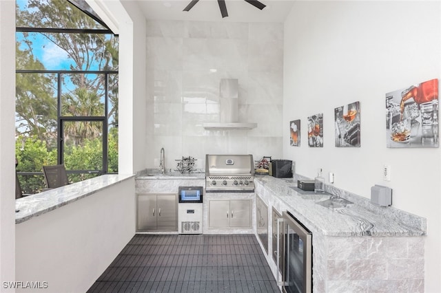 interior space with light stone counters, ceiling fan, wine cooler, sink, and wall chimney exhaust hood