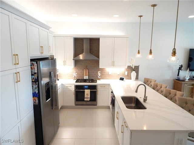 kitchen featuring a breakfast bar, stainless steel appliances, sink, light stone counters, and wall chimney range hood