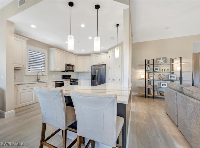 kitchen featuring light wood-type flooring, black appliances, a breakfast bar area, and decorative light fixtures