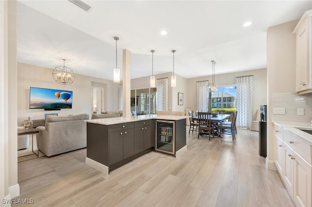 kitchen with wine cooler, a center island with sink, light hardwood / wood-style flooring, decorative backsplash, and white cabinetry