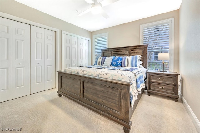 bedroom with light colored carpet, ceiling fan, and multiple closets