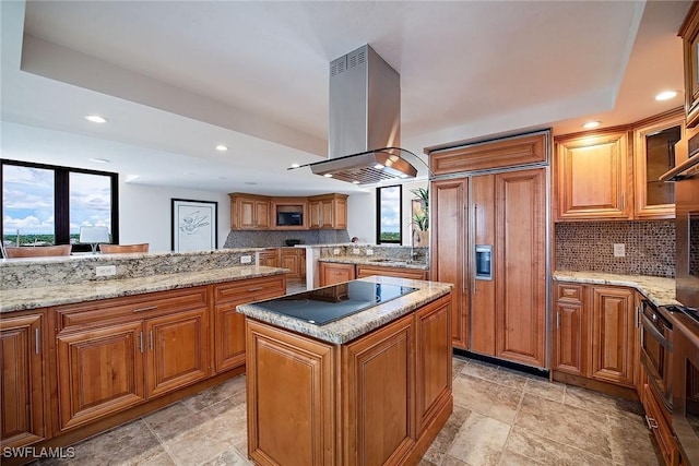 kitchen featuring brown cabinetry, a center island, island exhaust hood, black electric stovetop, and paneled fridge