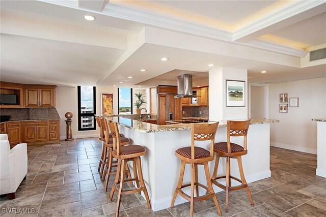 kitchen with crown molding, backsplash, a kitchen bar, kitchen peninsula, and island exhaust hood