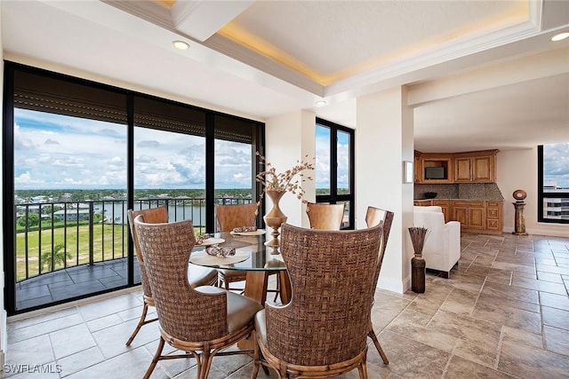 dining space with a water view, a raised ceiling, stone tile flooring, and baseboards