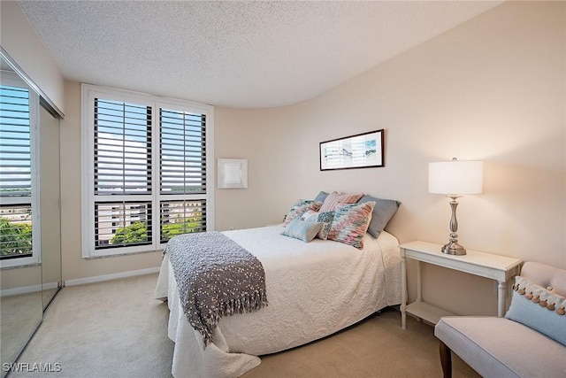 bedroom featuring light colored carpet, a textured ceiling, and baseboards