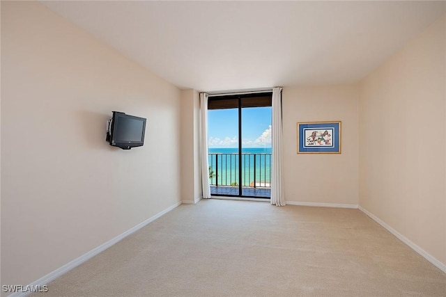 spare room featuring light carpet, floor to ceiling windows, and baseboards