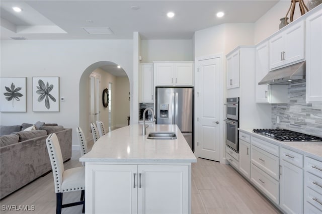 kitchen featuring arched walkways, appliances with stainless steel finishes, open floor plan, under cabinet range hood, and backsplash