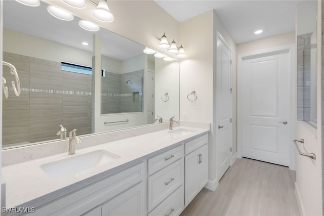 bathroom featuring wood finished floors, tiled shower, a sink, and double vanity