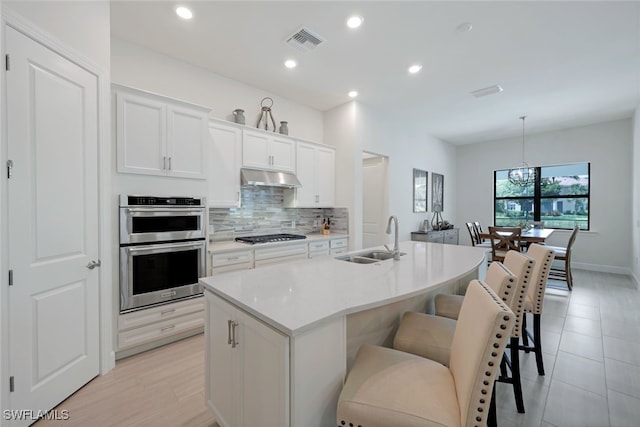 kitchen featuring under cabinet range hood, stainless steel appliances, a sink, visible vents, and backsplash