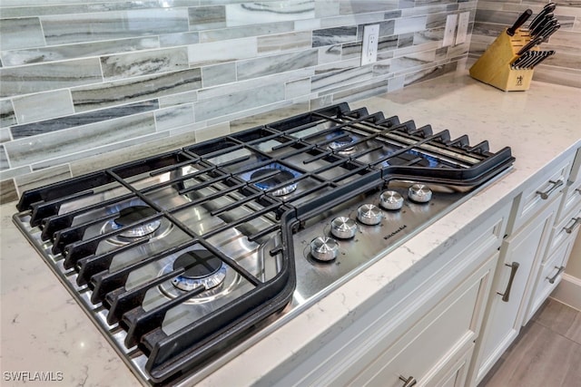 details with light stone counters, white cabinets, stainless steel gas stovetop, and decorative backsplash