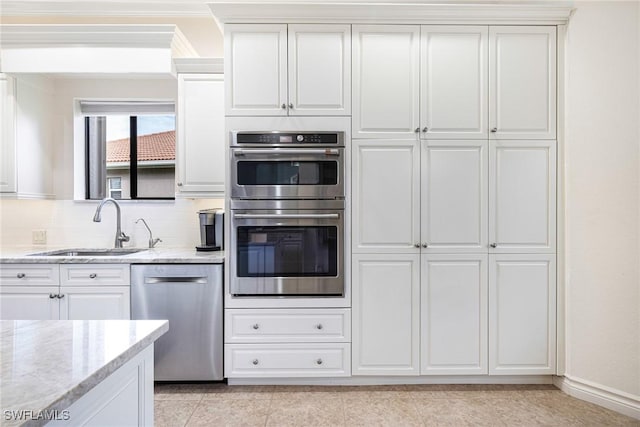 kitchen featuring appliances with stainless steel finishes, white cabinetry, light stone counters, and sink