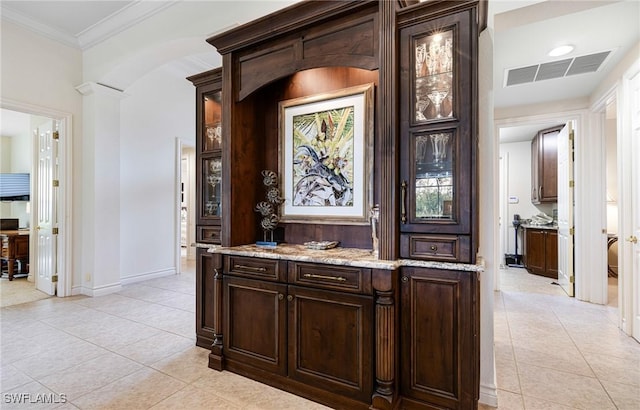 bar with light stone counters, ornamental molding, light tile patterned floors, and dark brown cabinetry